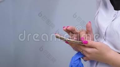 女人，穿着白色医用长袍的医生摘下橡胶手套，在手机上键入一些东<strong>西</strong>。 <strong>双</strong>手特写